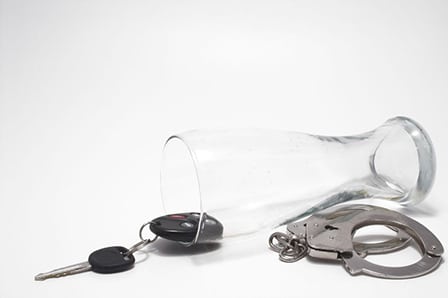 an empty beer glass with car keys and handcuffs illustrating a dwi